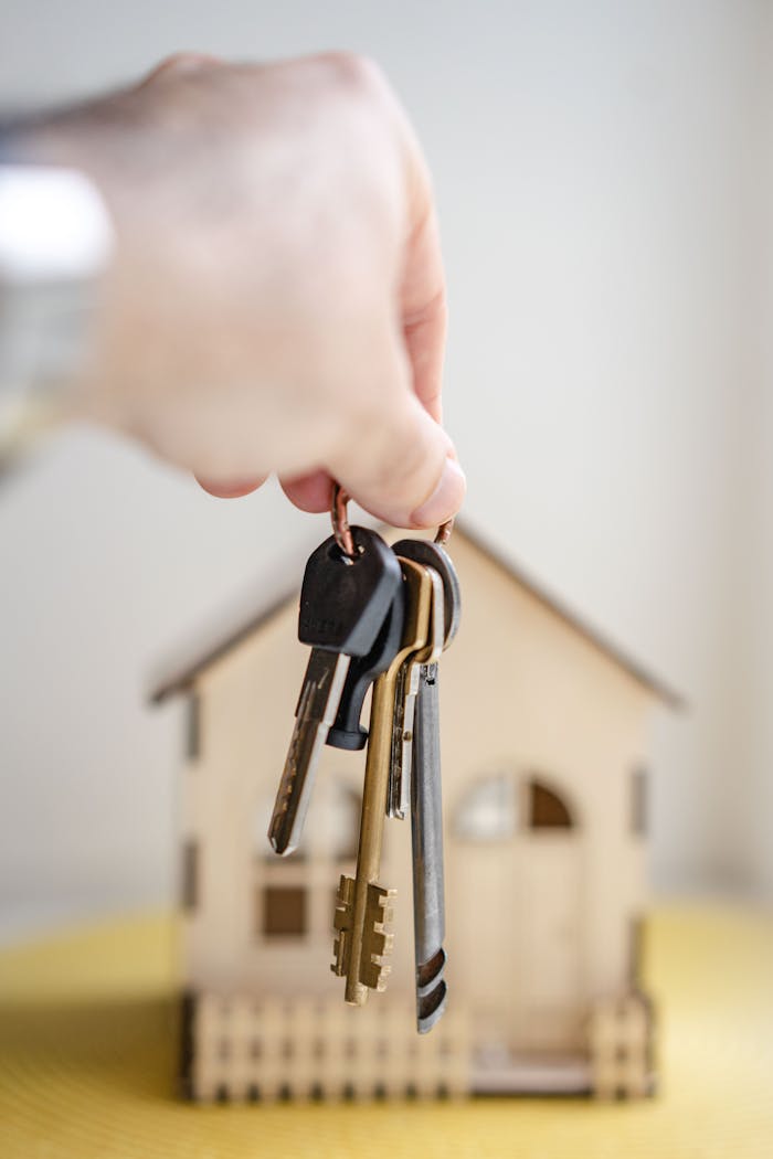 who-we-are Close-up of a hand holding keys with a miniature wooden house in the background, symbolizing real estate investment.
